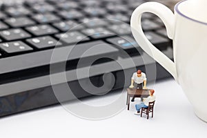 Miniature people sitting on table with keyboard and cup of coffee