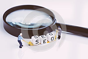 Miniature people staffs with forklift arrange cube block building the word SEO on magnifying glass using as Search Engine