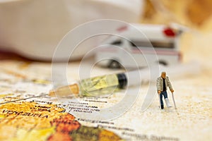 Miniature people stand on world map with ambulance car, medical mask and Syringe of COVID-19 vaccine .