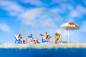 Miniature people sunbathing on The beach with blue sky background