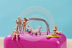Miniature people in swimsuit on a pink suitcase
