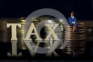 Miniature People. Tax concept.Word Tax and taxman sitting on stacked coins.. Macro photo