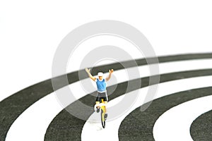 Miniature people toy figure photography. Bike cycling track. A biker cycling above dartboard, isolated on white background