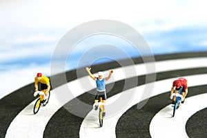 Miniature people toy figure photography. Bike cycling track. A biker cycling above dartboard, isolated on white background