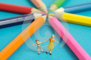 Miniature people toy figure photography. Drawing class concept. A group of kids playing on colorful pencil,  on blue