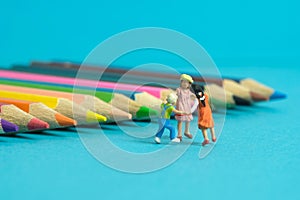 Miniature people toy figure photography. Drawing class concept. A group of kids playing on colorful pencil, isolated on blue