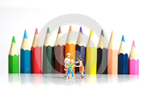 Miniature people toy figure photography. Drawing class concept. A group of kids playing on colorful pencil, isolated on white