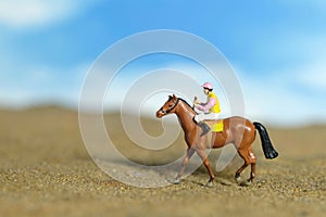 Miniature people toy figure photography. A jockey man riding horse at farm, sand desert land field