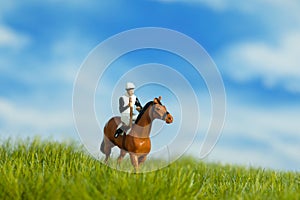 Miniature people toy figure photography. A jockey man riding horse at meadow field for training