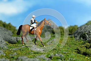 Miniature people toy figure photography. A jockey man riding horse at mountain hill for training