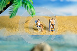 Miniature people toy figure photography. Men and girl couple relaxing on beach chair when daylight at seaside