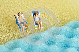 Miniature people toy figure photography. Men and girl relaxing at beach chair in front of wavy beach