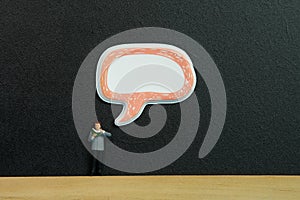 Miniature people toy figure photography. A men reading a book above chalkboard or black board with bubble message sticker