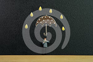 Miniature people toy figure photography. A men reading a book above chalkboard or black board with droplet and umbrella sticker