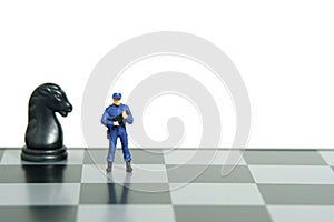 Miniature people toy figure photography. Protection strategy concept. A security officer standing above chessboard. Isolated on