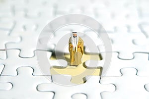 A Sultan wearing yellow Bisht (king cloak) standing above missing piece of puzzle jigsaw photo