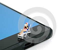 Miniature people toy figure photography. Virtual travel concept, Girl relaxing seat while reading book at chair above smartphone,