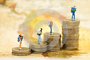 Miniature people: travelers with backpack standing on top stack of coins. Image use for travel business concept