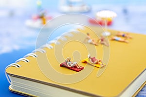 Miniature people: Travelers lie sunbathe on the book brown and blue ocean. Image use for vacation, summer, relax time concept