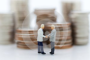 Miniature people : Two businessmen make a deal, with stack of coins to background,