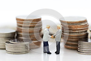 Miniature people : Two businessmen make a deal, with stack of coins to background, using as commitment, agreement, saving, finance