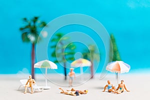 Miniature people wearing swimsuit relaxing on the beach