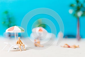 Miniature people wearing swimsuit relaxing on the beach