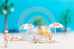Miniature people wearing swimsuit relaxing on the beach