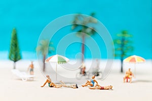 Miniature people wearing swimsuit relaxing on the beach