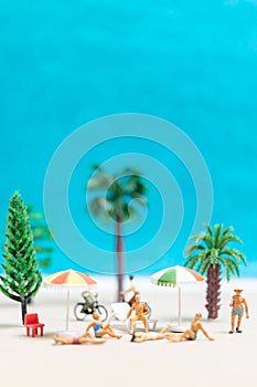 Miniature people wearing swimsuit relaxing on the beach