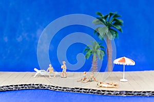 Miniature people wearing swimsuit relaxing on the beach