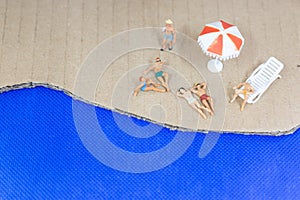 Miniature people wearing swimsuit relaxing on the beach