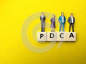 Miniature people with word PDCA on yellow background.