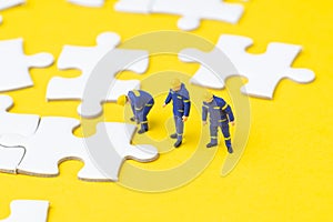 Miniature people worker team or staff help finishing white jigsaw puzzle pieces on yellow background with copy space, teamwork,