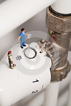 Miniature Plumbers Repairing A Thermostat.