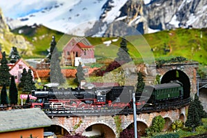Miniature railway model with model steam locomotive train that exit from a tunnel on a mountains ambientation. Toy Train