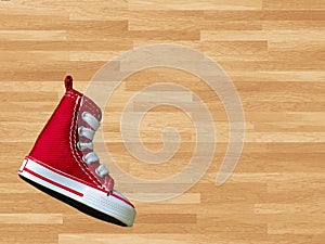 Miniature red baskeball shoe on wooden floor as background