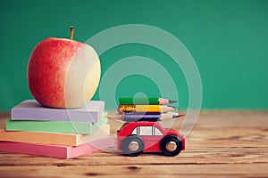 Miniature Red Car Carrying a colorful pencils and red apple and stack papers on wooden table. Back to school concept