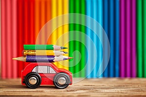 Miniature Red Car Carrying a colorful pencils on plasticine multi-colored wall. Back to school concept