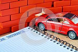 Miniature red car crashed in a brick wall and car insurance form