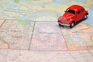 Miniature red car driving on a map of the pairie provinces, canada