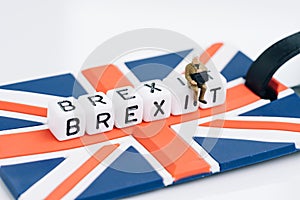 Miniature sad man sit on cube block with alphabets building the word BREXIT on union jack UK flag with white copy space background