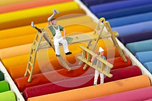 Miniature scale model painters and decorators with ladders on a set of oil pastel crayons.