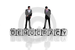 Miniature scale model politicians standing behind the word democracy