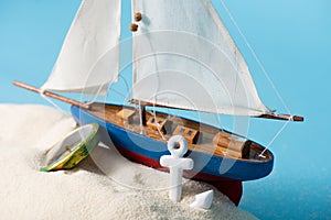 Miniature ship near compass and anchor in white sand is