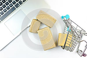 Miniature shopping cart and cardboard boxes spilled over laptop computer isolated on white