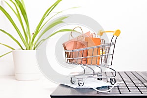 miniature shopping trolley on a black laptop stands, small paper bags in the trolley,