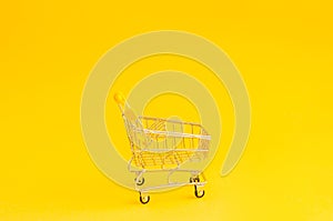 Miniature shopping trolley on a yellow background with place for text