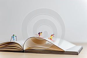 Miniature skiers sliding down the open book. Sport and travel concept