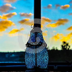 Miniature sky blue glass lantern lamp bauble against yellow orange southwest sunset glowing clouds